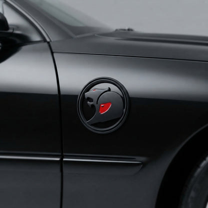 Black round 3D metal badge with red accent on the front fender of a black car, near the door seam