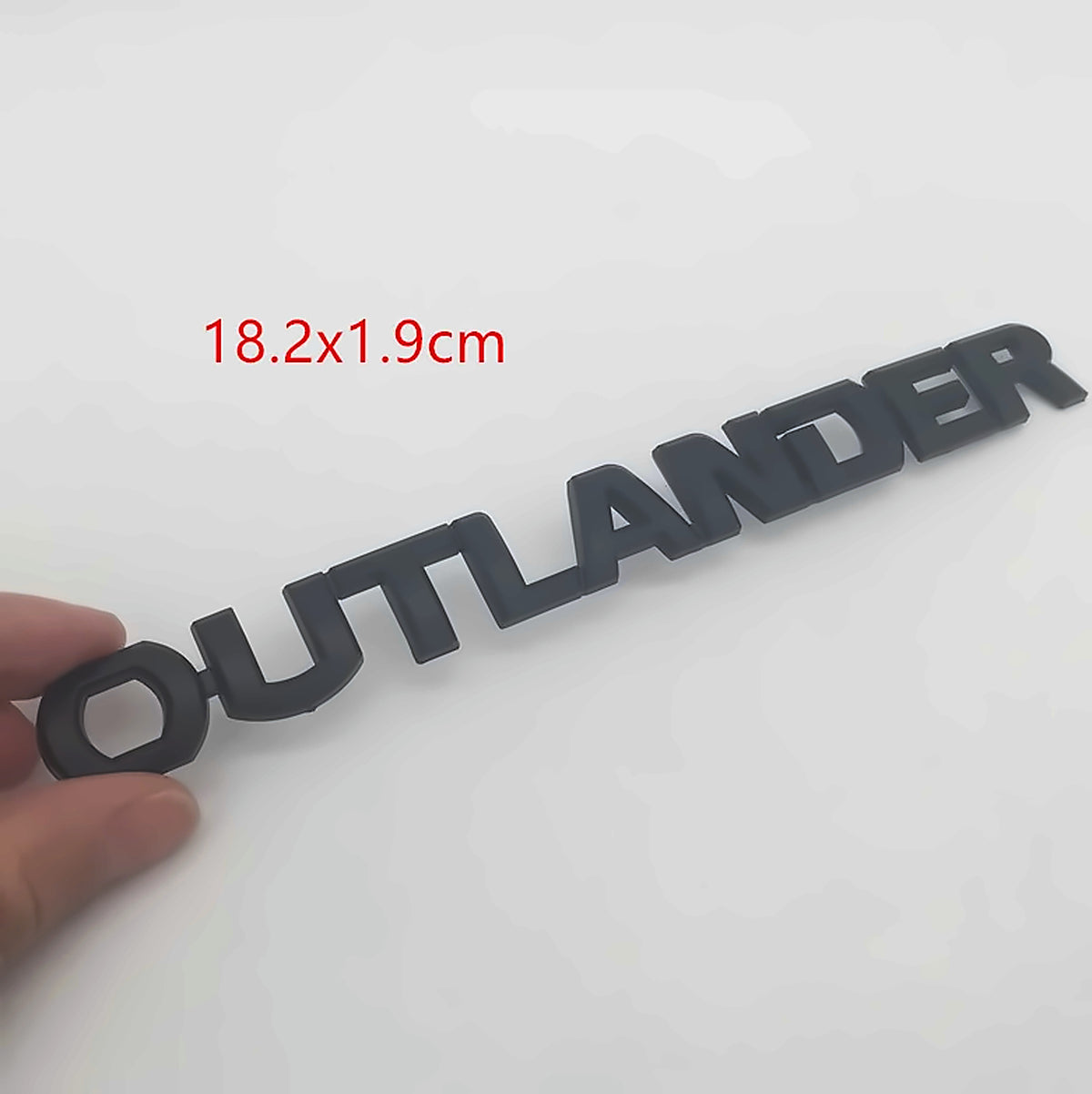 Matte black 3D Outlander letter emblem badge held in hand, labelled 18.2 x 1.9 cm