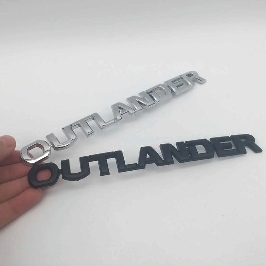 Mitsubishi Outlander 3D letter emblem badges in chrome silver and matte black, shown side by side